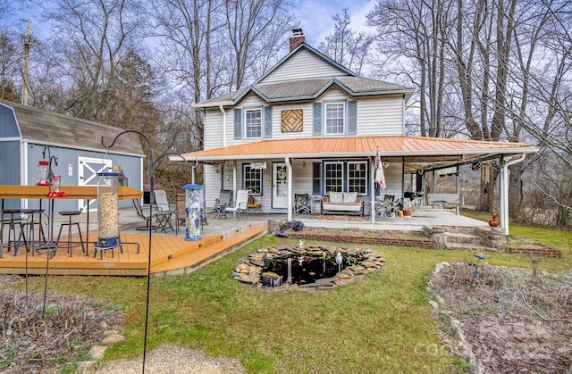 rear view of property featuring a yard, a chimney, a carport, an outdoor structure, and a wooden deck