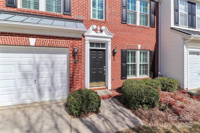 view of exterior entry featuring a garage and brick siding