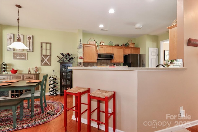 kitchen featuring wood finished floors, a kitchen breakfast bar, freestanding refrigerator, stainless steel microwave, and pendant lighting