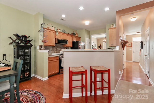 kitchen with light wood finished floors, visible vents, decorative backsplash, appliances with stainless steel finishes, and a kitchen bar