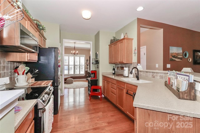 kitchen with appliances with stainless steel finishes, a peninsula, a sink, light wood-style floors, and a notable chandelier