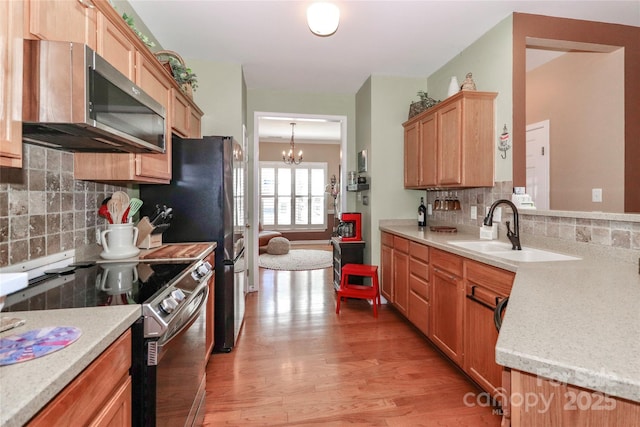 kitchen featuring light wood finished floors, tasteful backsplash, stainless steel appliances, a chandelier, and a sink