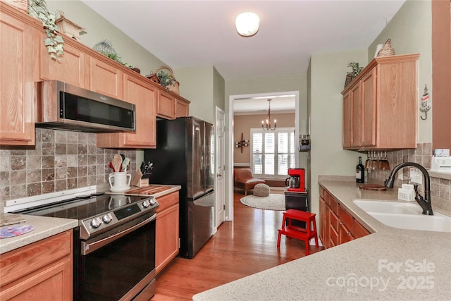 kitchen featuring light countertops, decorative backsplash, appliances with stainless steel finishes, light wood-style floors, and a sink