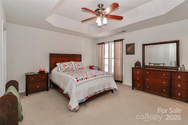 bedroom featuring carpet floors, a raised ceiling, visible vents, ceiling fan, and baseboards