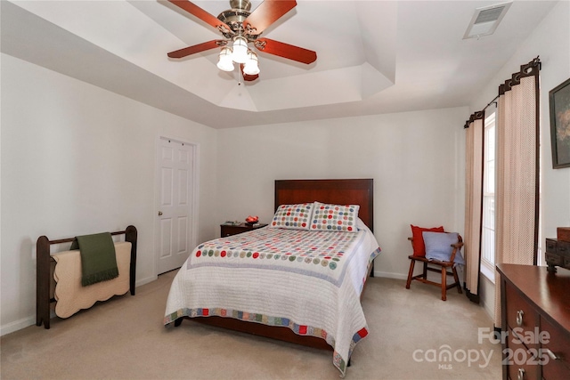 carpeted bedroom featuring a ceiling fan, a raised ceiling, visible vents, and baseboards