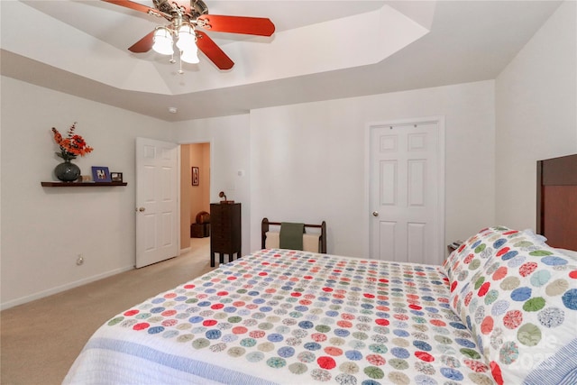 bedroom featuring light carpet, ceiling fan, a tray ceiling, and baseboards