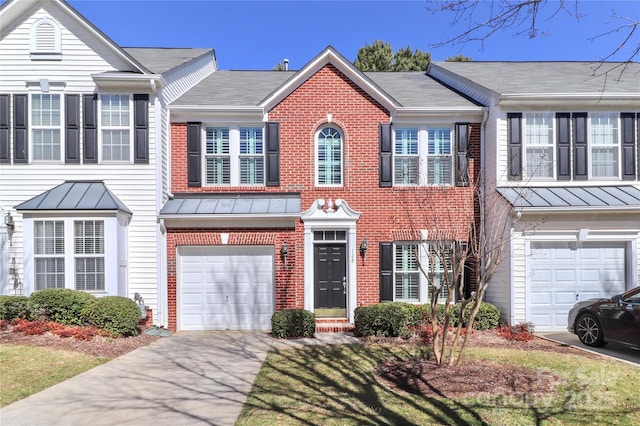 townhome / multi-family property with concrete driveway, brick siding, a standing seam roof, and an attached garage