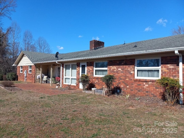 rear view of house with a chimney, a lawn, a patio, and brick siding