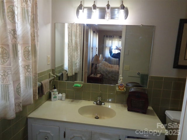 bathroom with toilet, wainscoting, tile walls, and vanity