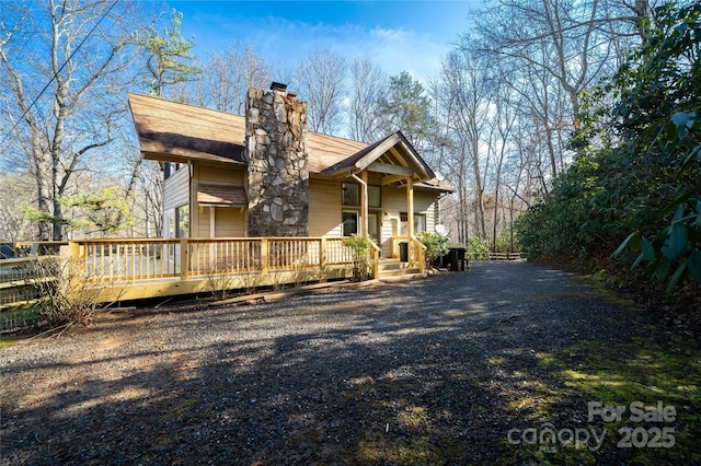 rustic home featuring a chimney, gravel driveway, and a wooden deck