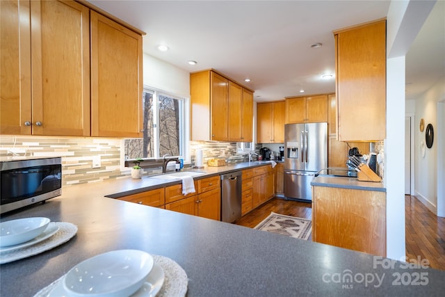 kitchen with appliances with stainless steel finishes, wood finished floors, a peninsula, a sink, and backsplash