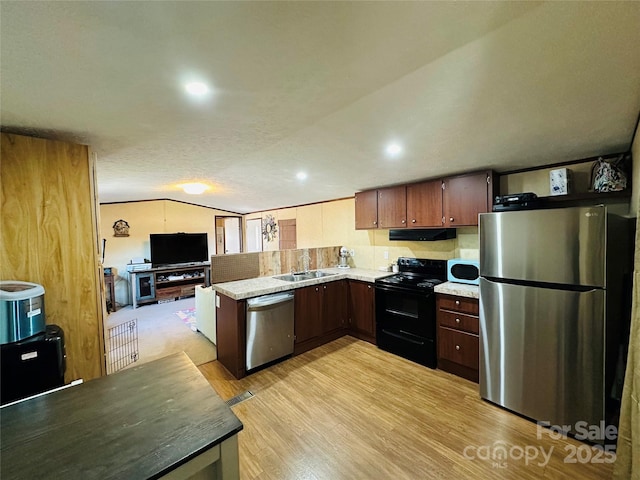 kitchen with vaulted ceiling, stainless steel appliances, light countertops, under cabinet range hood, and a sink