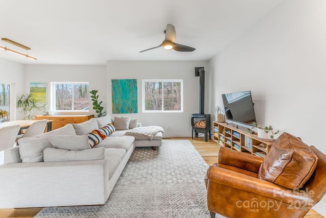 living area with a wood stove, light wood-style flooring, and ceiling fan