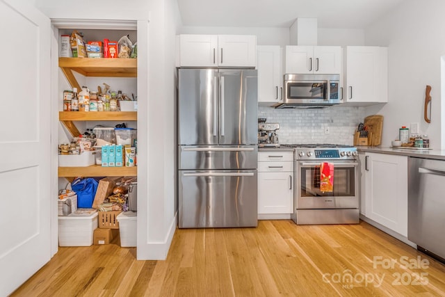 kitchen with light wood-type flooring, tasteful backsplash, appliances with stainless steel finishes, and white cabinetry