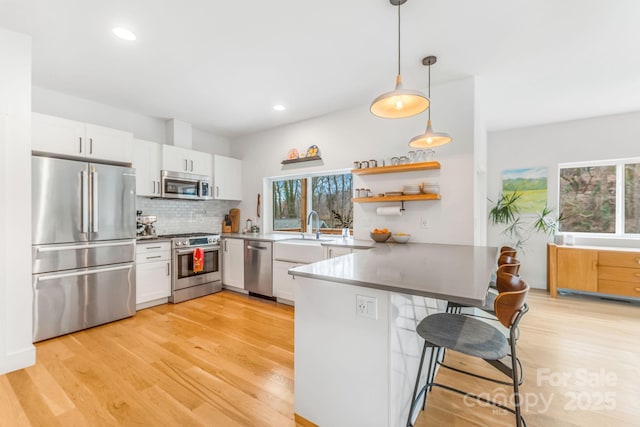 kitchen featuring appliances with stainless steel finishes, a peninsula, light wood-style floors, white cabinets, and a sink