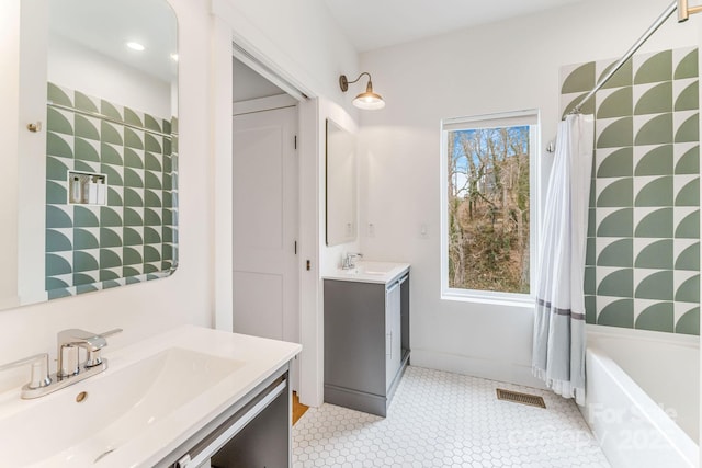 full bath featuring a bath, visible vents, two vanities, and a sink