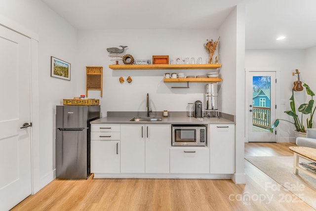 bar with baseboards, freestanding refrigerator, a sink, stainless steel microwave, and light wood-type flooring