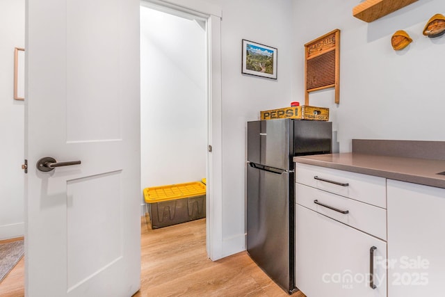 kitchen with light wood-style flooring, dark countertops, white cabinetry, freestanding refrigerator, and baseboards