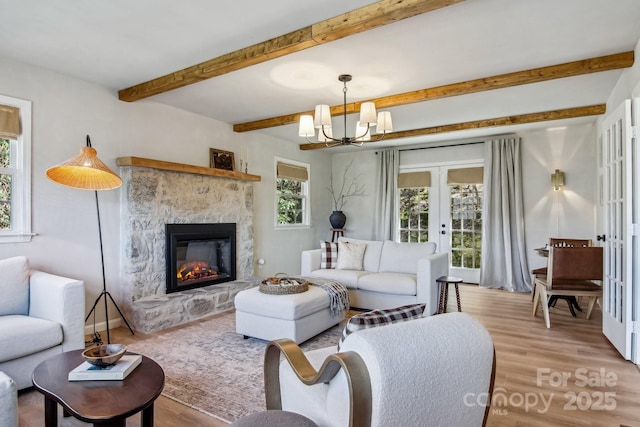 living room with a glass covered fireplace, beamed ceiling, french doors, light wood-style floors, and a notable chandelier