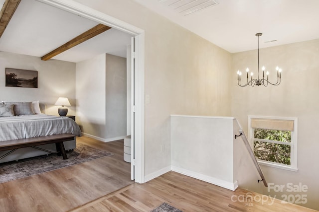 bedroom featuring a notable chandelier, wood finished floors, visible vents, baseboards, and beam ceiling