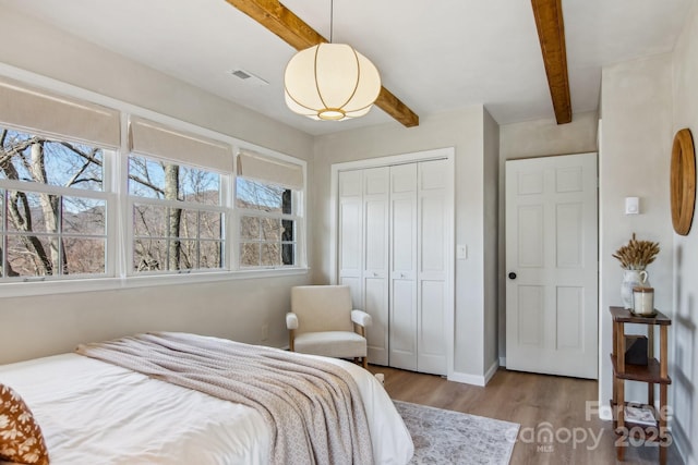 bedroom featuring baseboards, visible vents, beamed ceiling, wood finished floors, and a closet