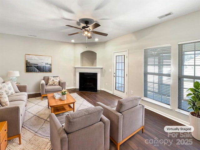 living area with ceiling fan, dark wood-style flooring, a fireplace, visible vents, and baseboards