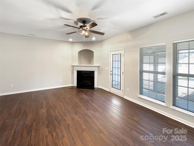 unfurnished living room featuring a fireplace, visible vents, dark wood-type flooring, a ceiling fan, and baseboards