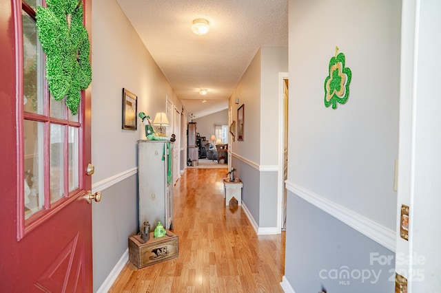 hall featuring a textured ceiling, light wood finished floors, and baseboards