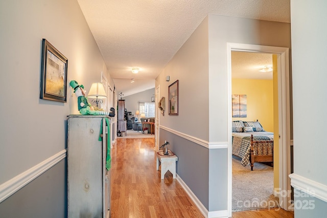 hall with light wood-style floors, vaulted ceiling, a textured ceiling, and baseboards