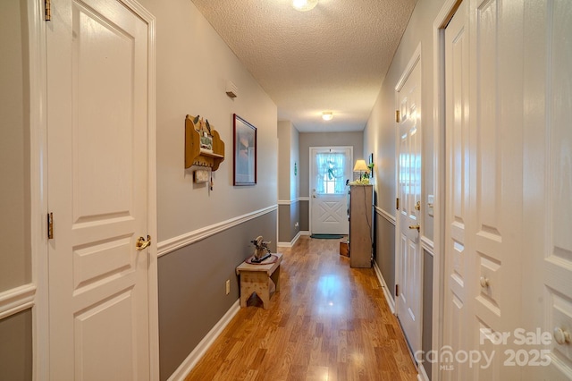 hallway featuring light wood-style floors, a textured ceiling, and baseboards