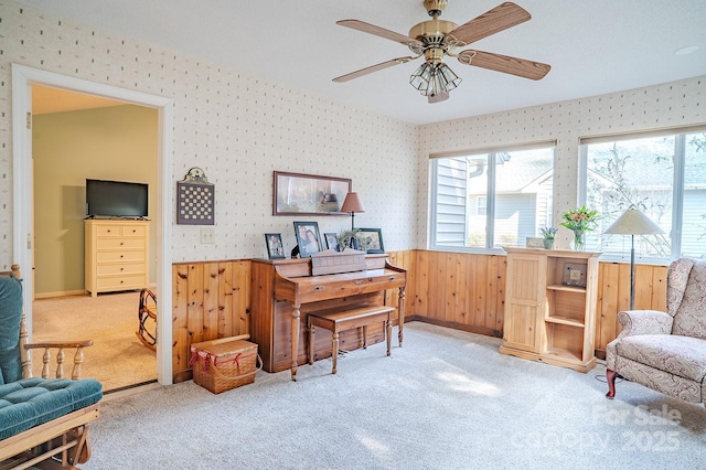 home office with a wainscoted wall, light carpet, a ceiling fan, and wallpapered walls