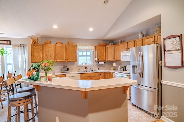 kitchen featuring white appliances, a sink, a kitchen breakfast bar, vaulted ceiling, and light countertops