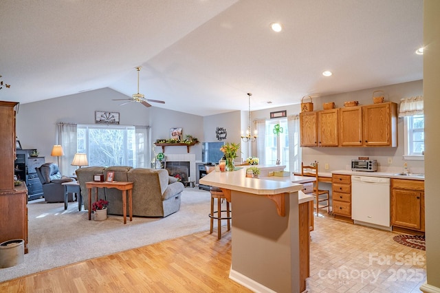 kitchen featuring lofted ceiling, white dishwasher, a fireplace, a kitchen breakfast bar, and light countertops