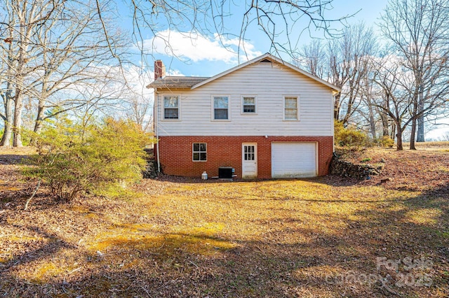 view of side of home featuring brick siding, a chimney, central air condition unit, a garage, and driveway