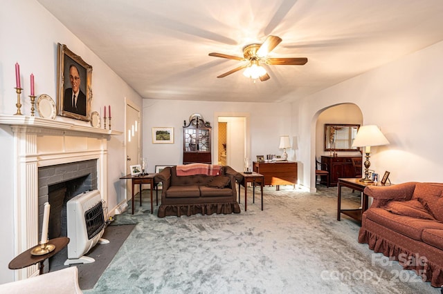 living area featuring arched walkways, heating unit, a fireplace with flush hearth, carpet flooring, and ceiling fan