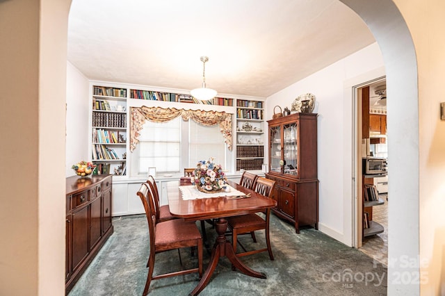 dining space with arched walkways and dark carpet