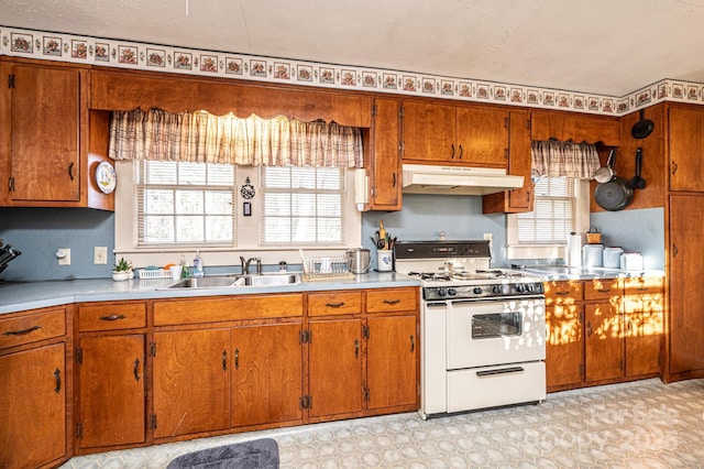 kitchen featuring under cabinet range hood, a sink, light countertops, white gas range oven, and light floors