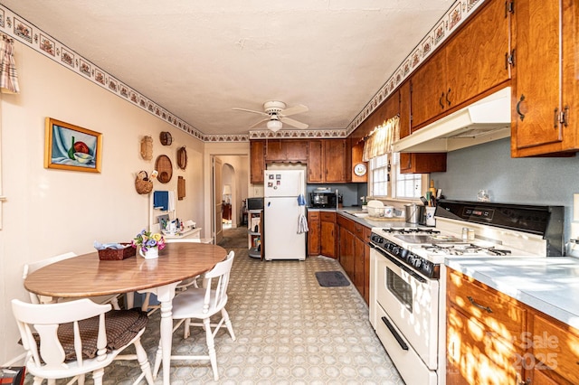 kitchen with white appliances, arched walkways, brown cabinets, light countertops, and under cabinet range hood