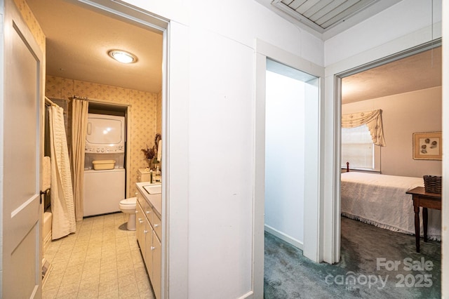 hallway featuring stacked washer / dryer, light floors, and wallpapered walls