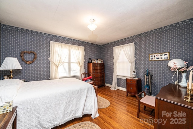 bedroom featuring wood finished floors, baseboards, and wallpapered walls