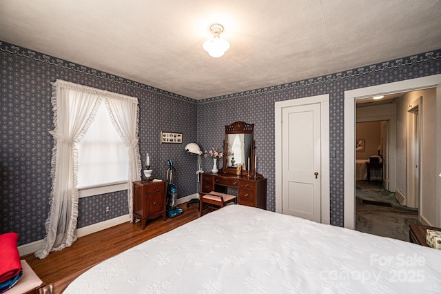 bedroom featuring baseboards, dark wood finished floors, and wallpapered walls