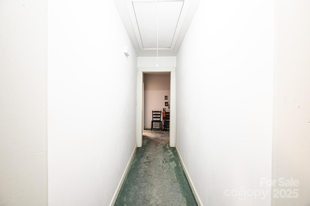 corridor featuring attic access, dark carpet, and baseboards