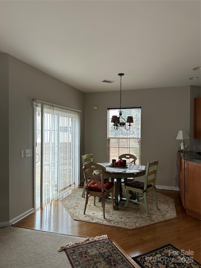 dining space featuring baseboards, wood finished floors, visible vents, and an inviting chandelier