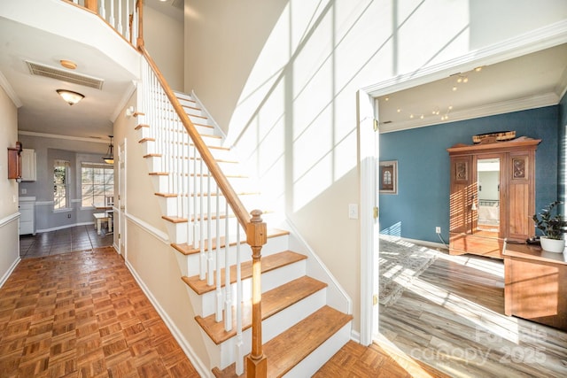 stairs featuring baseboards, a towering ceiling, visible vents, and crown molding