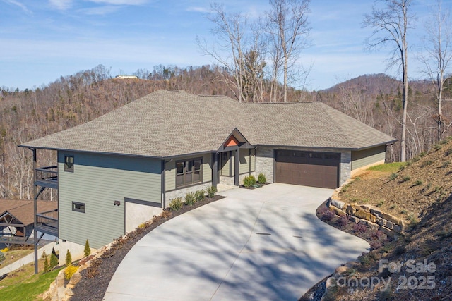 view of front facade featuring stone siding, a shingled roof, an attached garage, and driveway