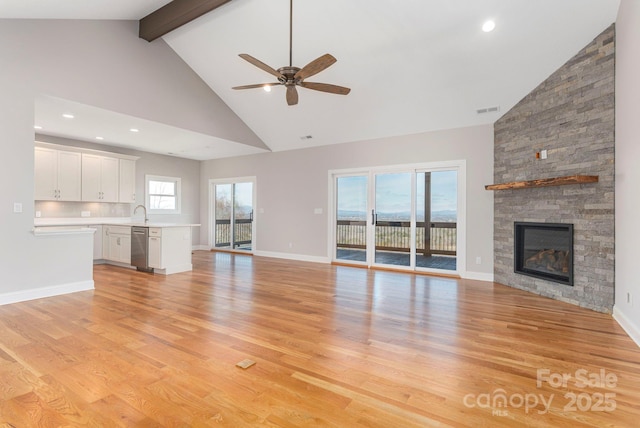 unfurnished living room with light wood-style flooring, ceiling fan, a stone fireplace, high vaulted ceiling, and beamed ceiling