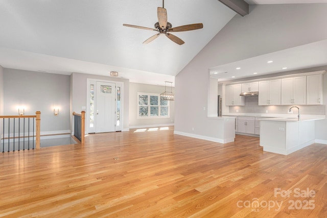 unfurnished living room featuring baseboards, light wood-style flooring, ceiling fan, beamed ceiling, and high vaulted ceiling