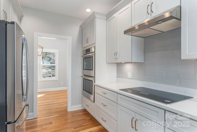 kitchen with tasteful backsplash, stainless steel appliances, light countertops, under cabinet range hood, and white cabinetry