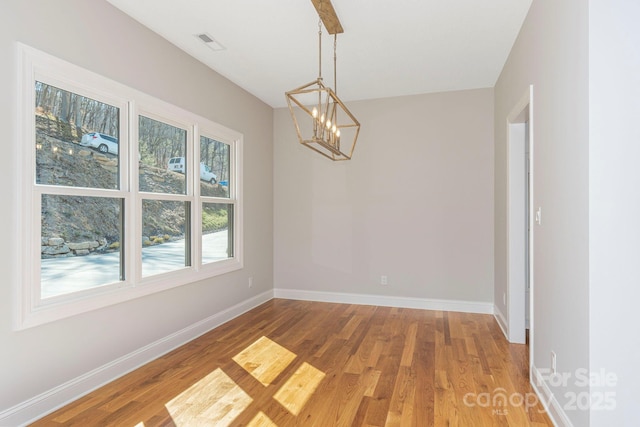 spare room with visible vents, a notable chandelier, baseboards, and wood finished floors