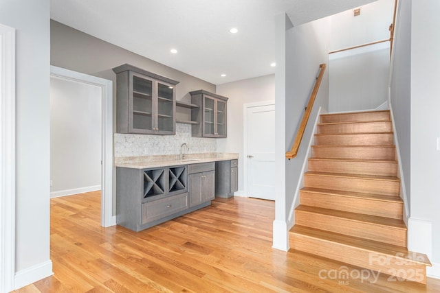 kitchen featuring decorative backsplash, glass insert cabinets, light countertops, light wood-style floors, and a sink